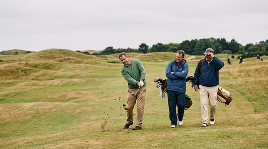A golfer mid-swing as dirt flies, two friends watching with amused expressions